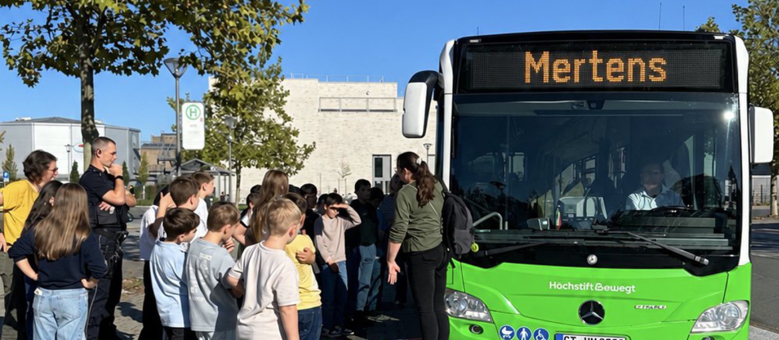 Eine Gruppe Kinder steht um einen Bus herum und wird von Fachpersonal eingewiesen.