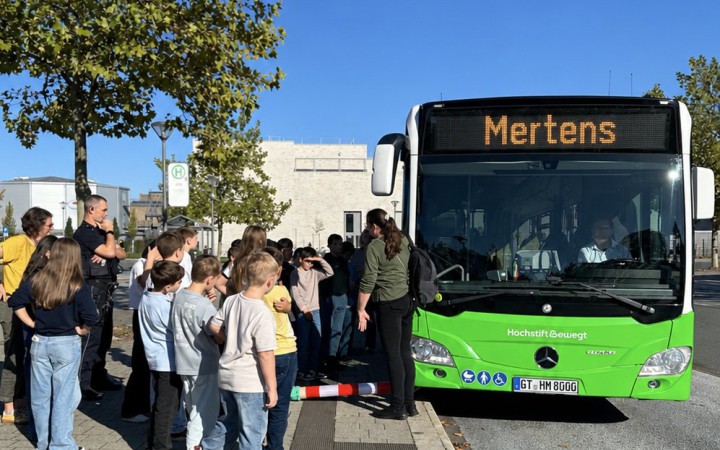 Eine Gruppe Kinder steht um einen Bus herum und wird von Fachpersonal eingewiesen.