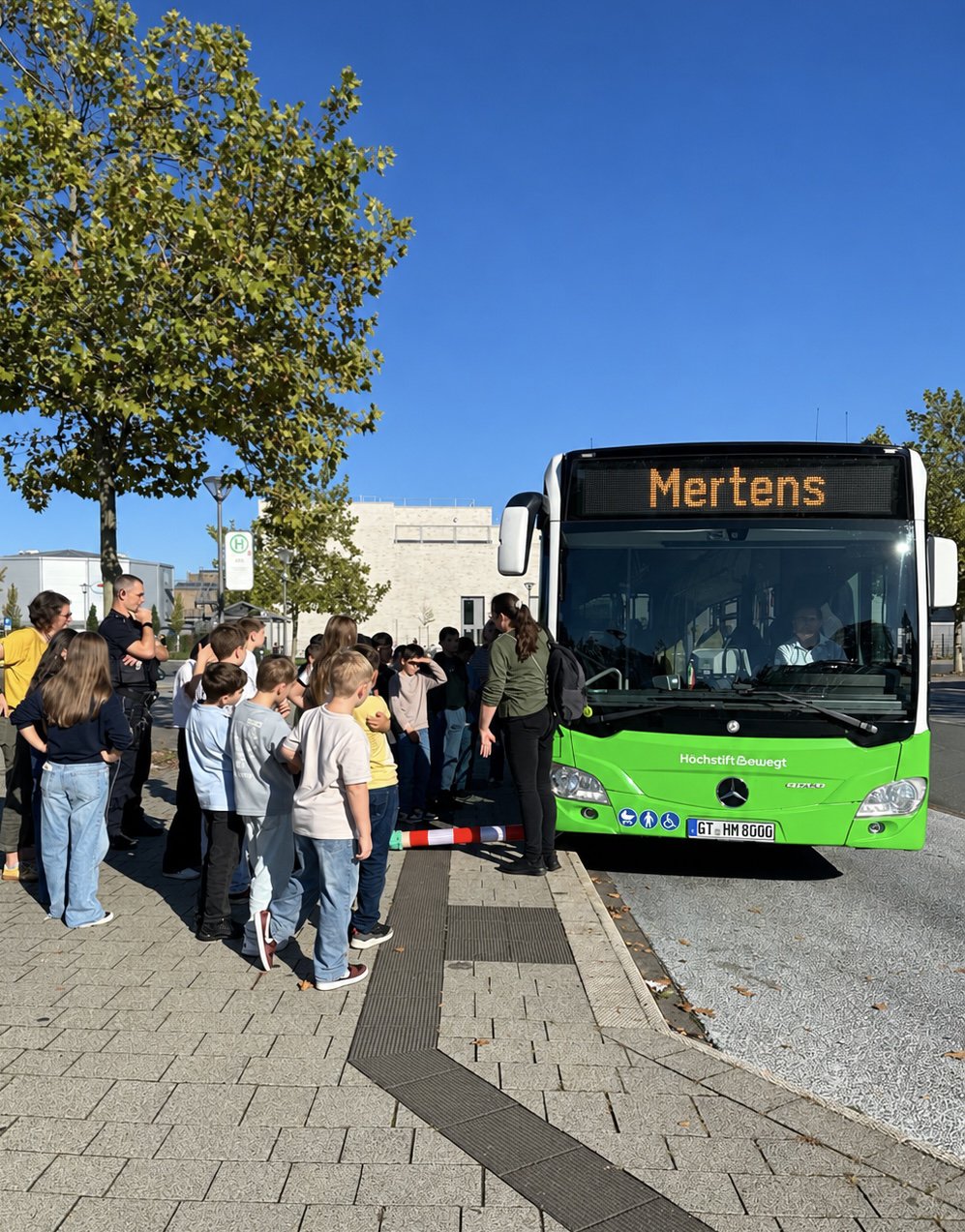 Eine Gruppe Kinder steht um einen Bus herum und wird von Fachpersonal eingewiesen.