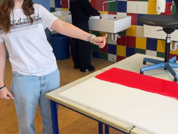 Eine Schülern steht neben ihrem Kunstprojekt und hebt bestätigend den Daumen.