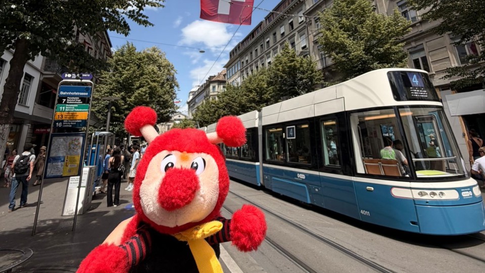 Schulmaskottchen Rieti vor einer Straßenbahn und der Schweizer Flagge in Zürich