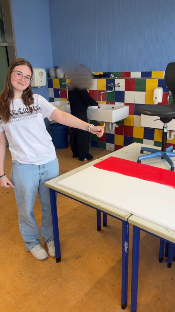 Eine Schülern steht neben ihrem Kunstprojekt und hebt bestätigend den Daumen.